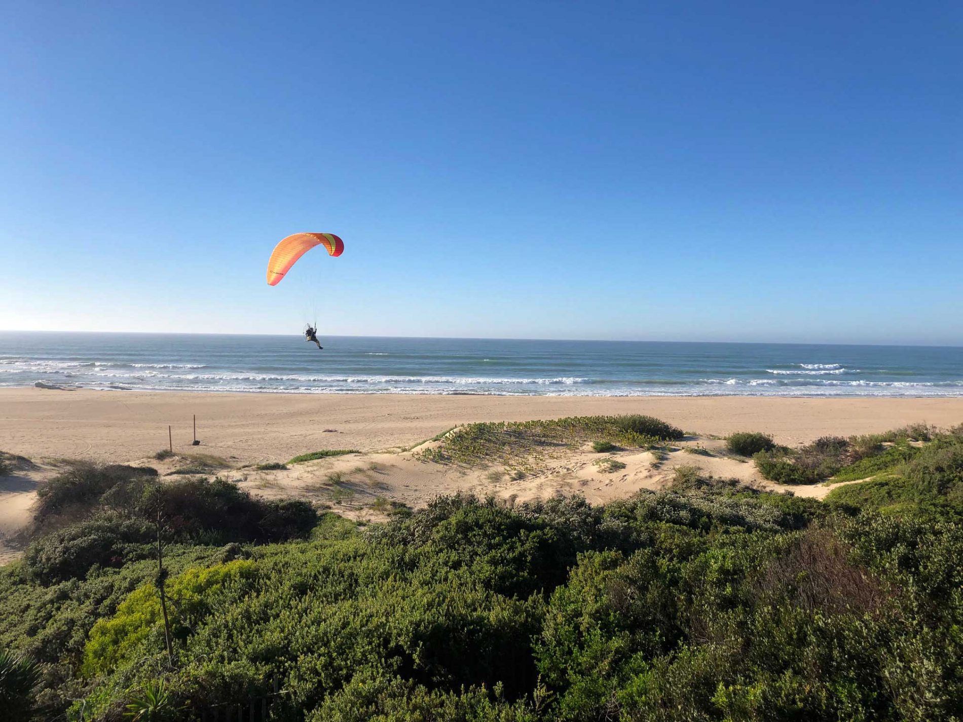Ein Paraglider fliegt über Jeffresy Bay